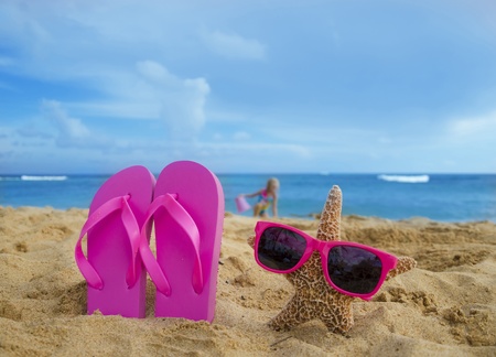 Girl's Flip flops and starfish with sunglasses on sandy beach with playing girl by the ocean on the background in Hawaiiの写真素材