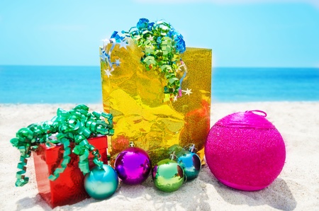 Gold gift bag and red gift box with Christmas balls on sandy beach in sunny day- holiday conceptの写真素材