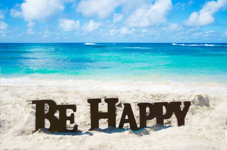 Sign "Be Happy" on the sandy beach by the ocean in sunny dayの写真素材