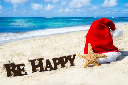 Sign Be Happy and starfish with christmas hat on the sandy beach by the ocean in sunny day