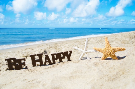 Sign "Be Happy" and two starfishes on the sandy beach by the ocean in sunny dayの写真素材