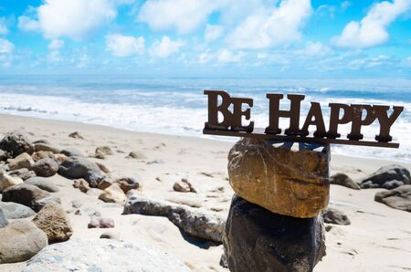 Sign "Be happy" on the top of rocks balancing by Pacific ocean の写真素材