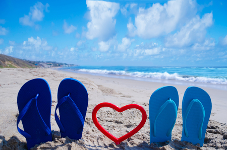 Flip flops with heart shape on the sandy beach by the oceanの写真素材