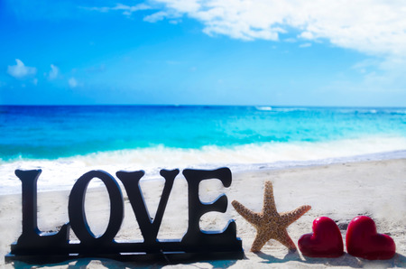 Sign "Love" with two heart shapes and starfish on the sandy beach by the oceanの写真素材