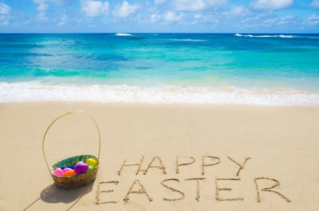 Sign "Happy Easter" with basket and eggs on the sandy beach by the oceanの写真素材