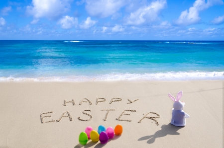 Sign "Happy Easter" with bunny and color eggs on the sandy beach by the oceanの写真素材