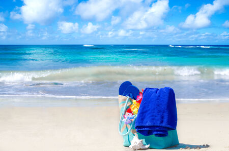 Beach bag with seashell, flip flops, and towel by the oceanの写真素材