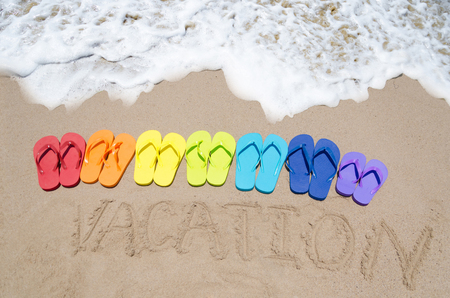 Sign "Vacation" and color flip flops on sandy beach by the ocean in sunny dayの写真素材