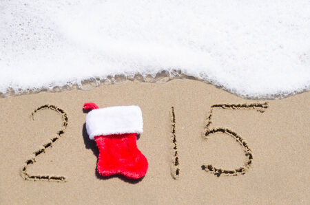 Sign 2015 with Christmas sock on the sandy beach by the ocean
