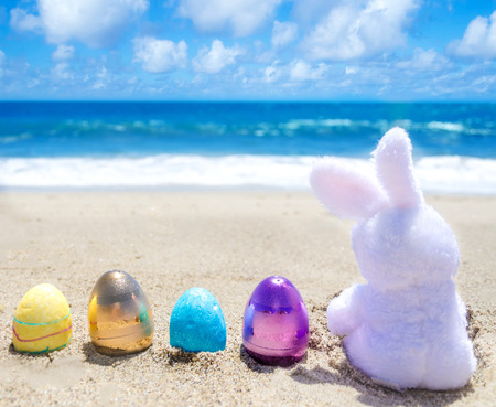 Easter bunny with color eggs on the sandy beach near oceanの写真素材
