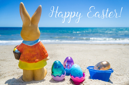 Easter bunny with color eggs on the sandy beach near ocean