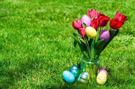 Easter Colorful eggs  and bright red tulips on the green grass background - spring moodの写真素材