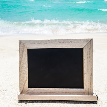 Empty black wood chalkboard on the sandy beach near the oceanの写真素材