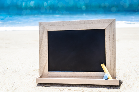 Empty black wood chalkboard with chalk on the sandy beach near the oceanの写真素材