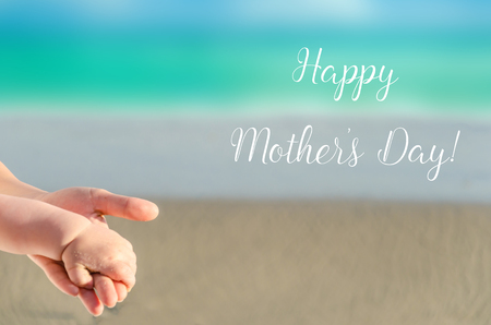 Happy Mother's day background with Mother's and child's holding hands on the sandy beach near ocean の写真素材