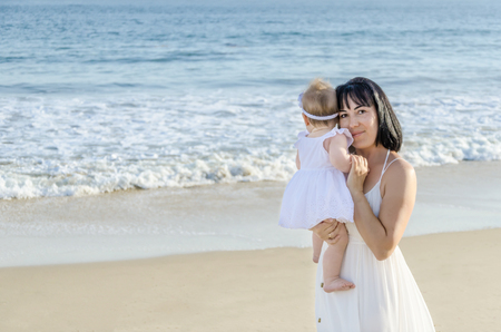Mother and her baby girl on the sandy beach near ocean in sunny day/Mothers day conceptの写真素材