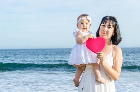 Mother and her baby girl on the sandy beach near ocean in sunny day/Mothers day conceptの写真素材