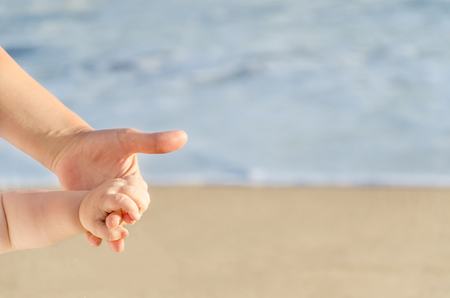 Mother is holding child's hand on the sandy beach near ocean in sunny day/Mothers day conceptの写真素材