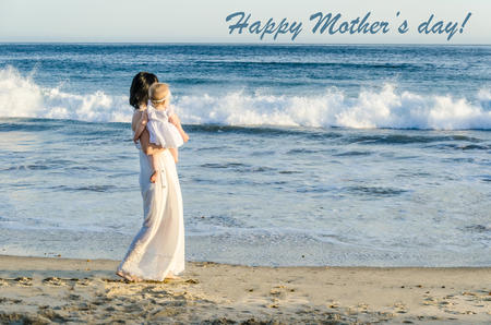 Happy Mother's day background with Mother and daughter on the sandy beach near ocean in sunny dayの写真素材