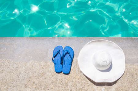 White summer hat and blue flip flops near the swimming pool