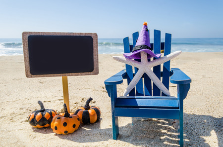 Halloween background with starfishes in the witch's hats and black board on the sandy beach near the oceanの写真素材