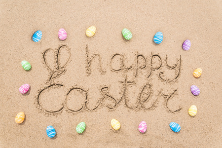 Happy easter background with eggs on the sandy beach near ocean. Hand drawn Happy Easter typography lettering sign.の写真素材