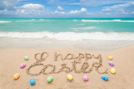 Happy easter background with eggs on the sandy beach near ocean. Hand drawn Happy Easter typography lettering sign.の写真素材