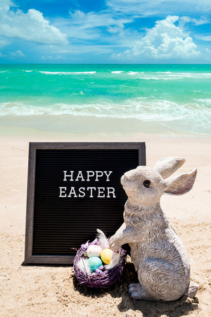Happy Easter beach background with black board and bunny with eggs near oceanの写真素材