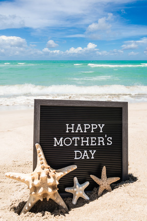 Happy Mother's day   with black board and starfishes on the sandy beach near the ocean.の写真素材
