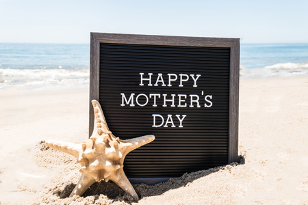 Happy Mother's day   with black board and starfish on the sandy beach near the ocean.の写真素材
