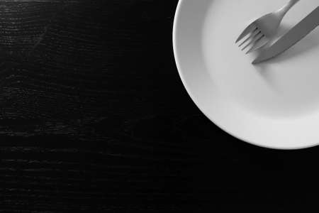 Empty white plate on black wooden table. Kitchen tools close upの写真素材