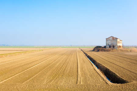 Rural Italian landscape from Po river lagoon.Plowed fields with perspective lines. Abandoned warehouseの写真素材
