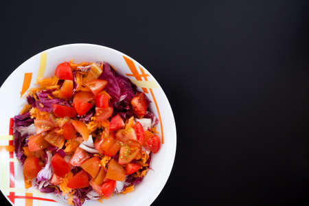 Salad with carrots and tomatoes on black table, top view. Food background