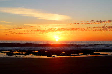 Beach sunset with bright orange sun. Waves and beach in foreground.
