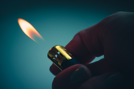 Lighter finger bright burning fire on dark green blue backgroundの写真素材