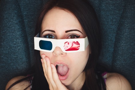 Girl with 3D glasses watches movie with shocked face in cinema close upの写真素材