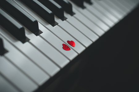 Two small red hearts on the white black keyboard of classic piano close up. Concept of love and romantic music. Copy spaceの写真素材