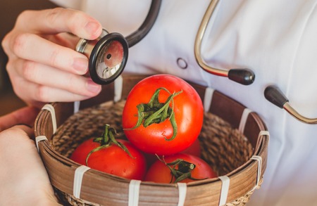 Doctor holds a stethoscope and checks up a tomato close up concept of control of harvest qualityの写真素材