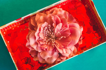 Gift box with small red hearts and flower barrette on green blue background top view close up