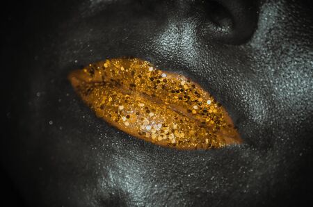 Gold lips with glitter close-up female face on dark background. Trendy colours conceptの写真素材
