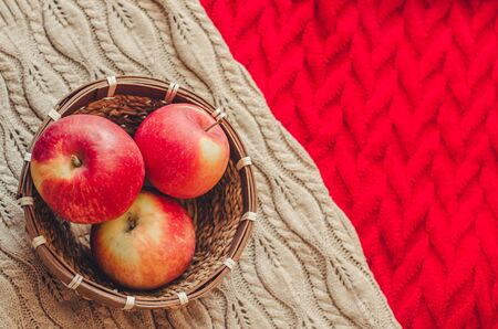 Three apples in the basket on knitted background. Concept of cozy autumn mood and harvestの写真素材