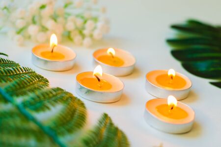 Five burning candles with small bouquet and green leaves on white background close-up. Relaxation and aromatherapy conceptの写真素材
