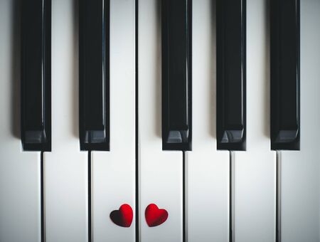 Two small red hearts on the white black keyboard of classic piano close-up. Concept of love and romantic music. Copy spaceの写真素材