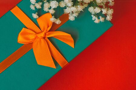 Gift with ribbon and white flowers lie on red background top view copy space minimalistic greeting cardの写真素材