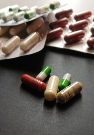 Close-up of assorted capsules in various colors, including red, green-white, beige, and brown,...