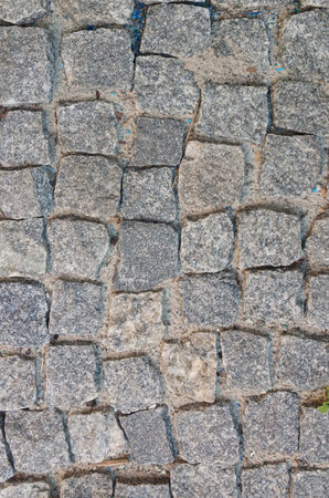 High-resolution photo of an old stone pavement with irregular granite blocks. The surface shows natural textures, cracks, and signs of time, creating a rustic and authentic background. Perfect for use in architectural projects, design mockups, textures, or as a natural stone background for creative works.の写真素材