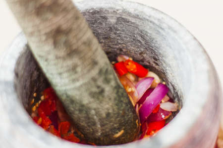 A mortar and pestle or lesung batu in Malay with crushed chilies, fried shallots and shrimp paste mixed together. Soft focus, shallow depth of field.の写真素材