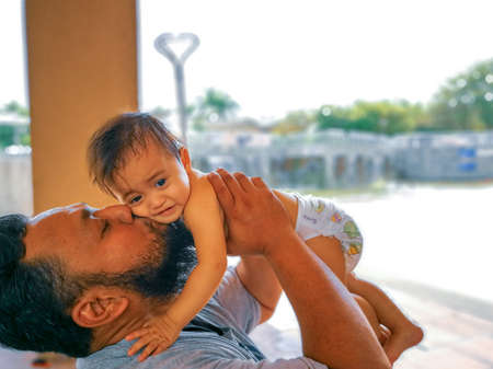 Father kissing baby on cheek while holding her in the park.の写真素材