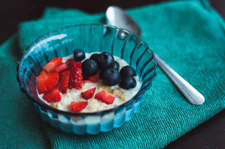 High angle view on cooked oat with forest fruits. Strawberries and blueberries in a blue glass bowl...