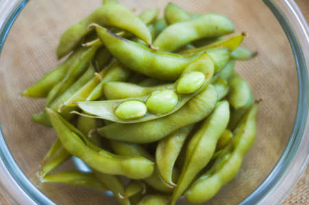 Close up portrait of Japanese food edamame nibbles, boiled green soybeans in a bowl on a burlap background.の写真素材